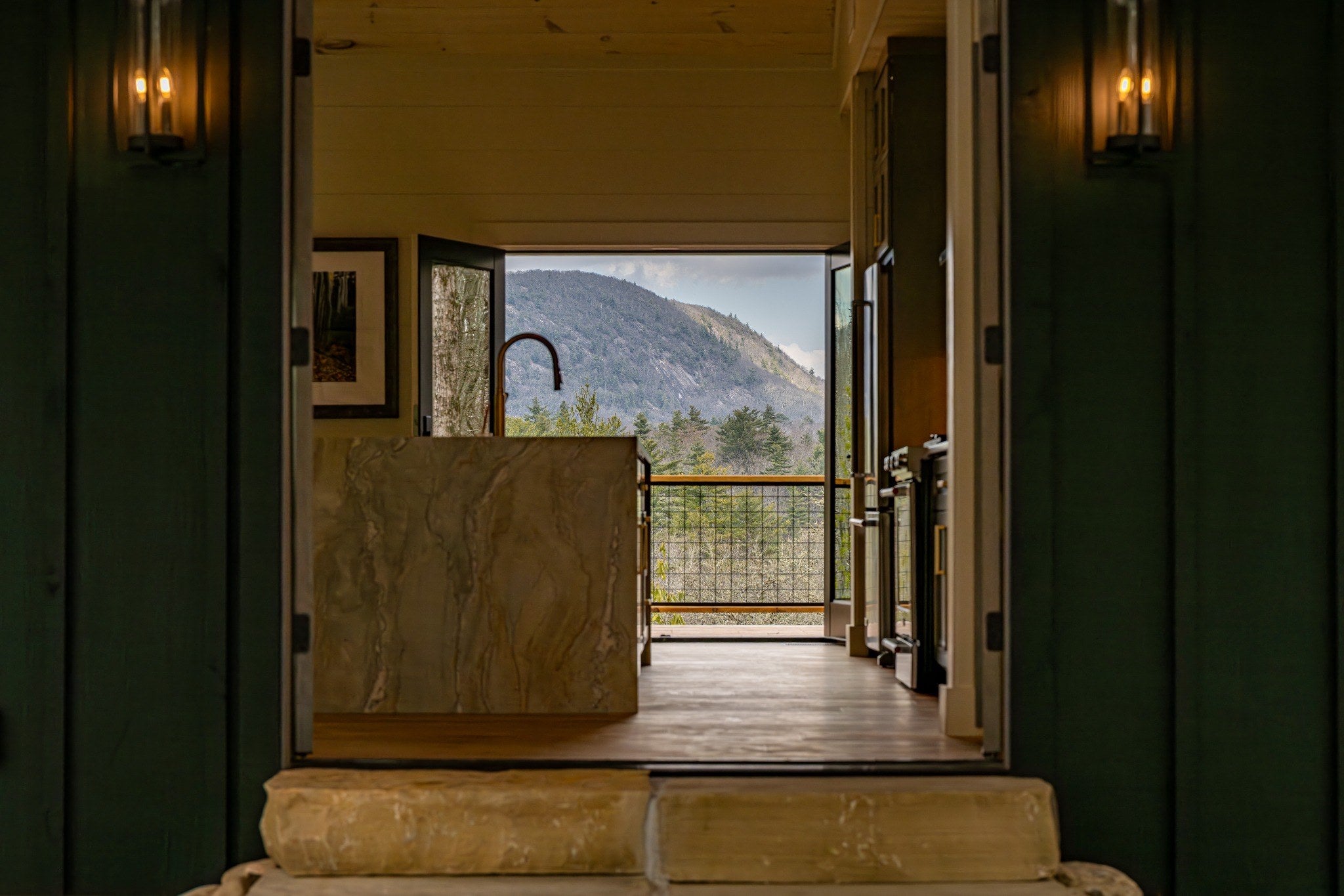 Open mountain home framed by natural stone, warm wood and deep green walls with a forested mountain beyond
